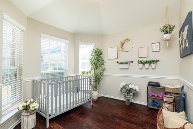 bedroom with a crib, lofted ceiling, and dark hardwood / wood-style flooring