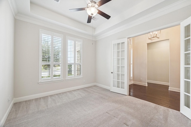 carpeted spare room with ornamental molding, a tray ceiling, ceiling fan with notable chandelier, and french doors