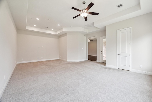 carpeted spare room with a raised ceiling and ceiling fan