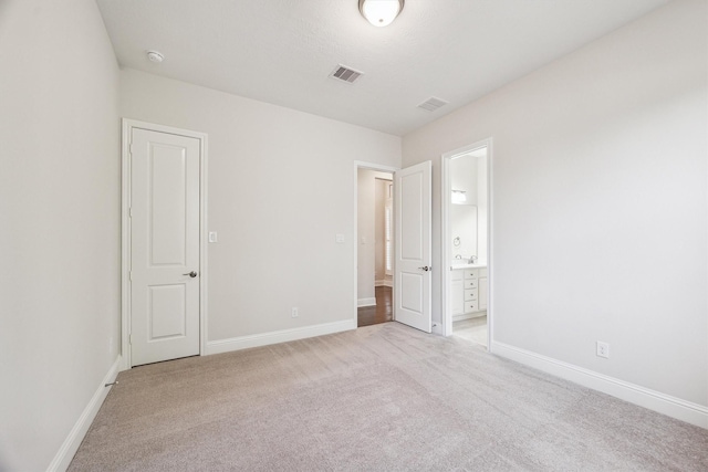 unfurnished bedroom featuring ensuite bath and light colored carpet