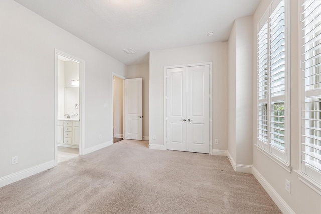 unfurnished bedroom with sink, light colored carpet, ensuite bath, and a closet