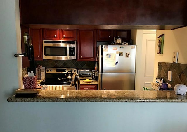 kitchen featuring sink, stainless steel appliances, light stone counters, decorative backsplash, and kitchen peninsula