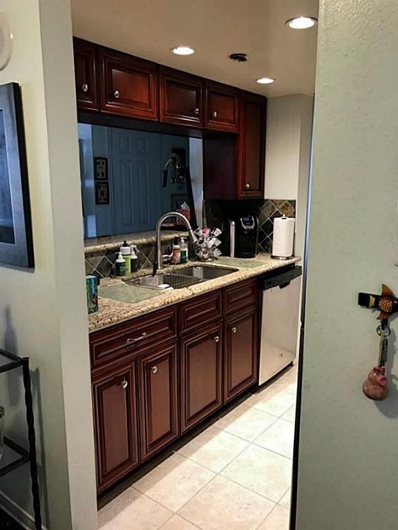 kitchen with sink, backsplash, stainless steel dishwasher, light tile patterned floors, and light stone countertops