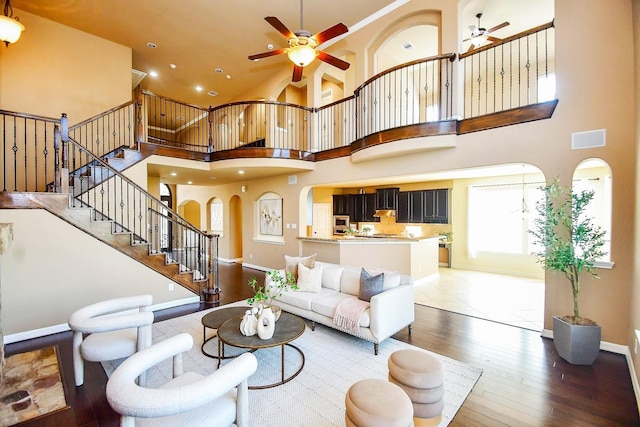 living room featuring ceiling fan, wood-type flooring, and a towering ceiling