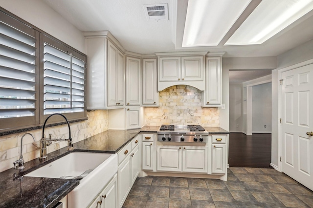 kitchen with tasteful backsplash, sink, dark stone countertops, and stainless steel gas stovetop