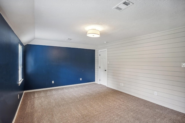 empty room featuring wooden walls, lofted ceiling, carpet flooring, and a textured ceiling