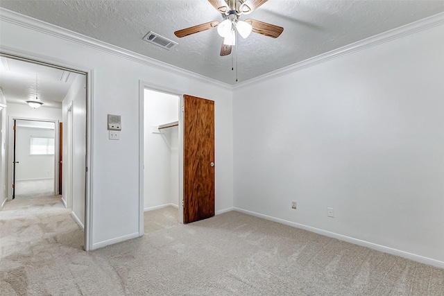 unfurnished bedroom with a walk in closet, ornamental molding, light carpet, and a textured ceiling