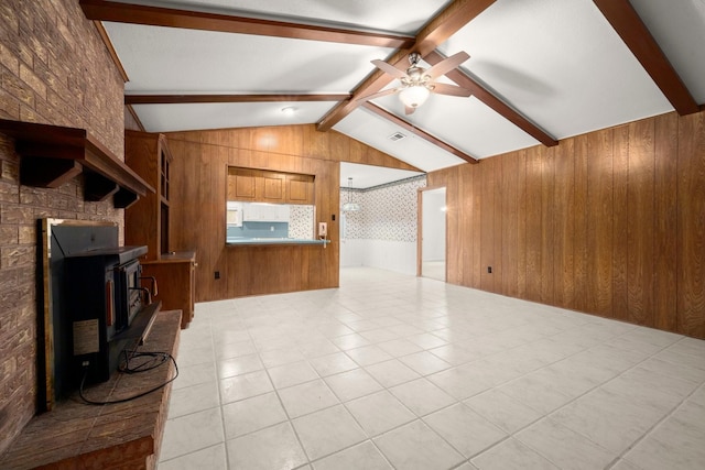 living room with wooden walls, lofted ceiling with beams, a wood stove, light tile patterned floors, and ceiling fan