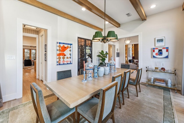 dining space featuring beam ceiling, light hardwood / wood-style floors, and a chandelier