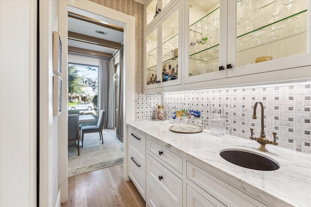 bar featuring sink, white cabinetry, backsplash, light stone counters, and light wood-type flooring