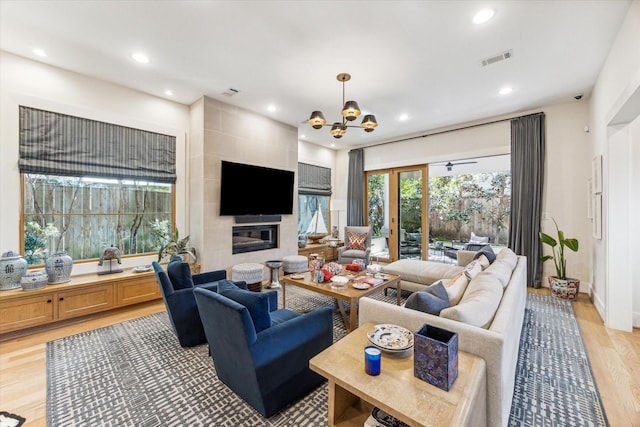 living room featuring a chandelier, a tiled fireplace, and light hardwood / wood-style flooring