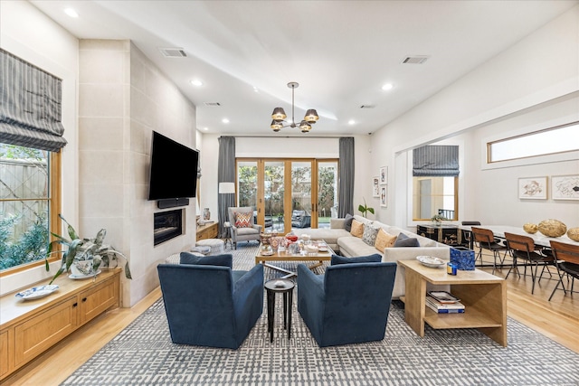 living room with a chandelier, a tiled fireplace, hardwood / wood-style floors, and french doors