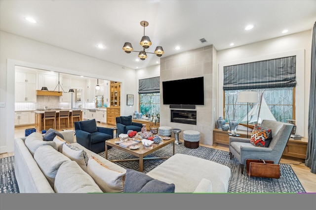 living room with light wood-type flooring, a tile fireplace, and a notable chandelier