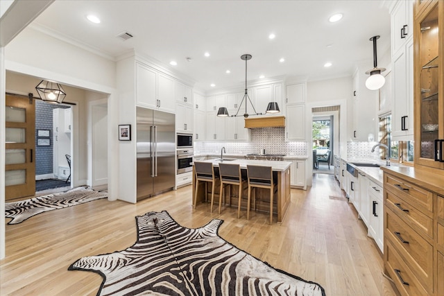 kitchen featuring a kitchen breakfast bar, a center island, built in appliances, white cabinets, and decorative light fixtures