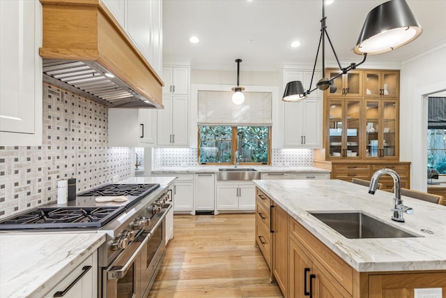 kitchen featuring premium range hood, sink, white cabinetry, decorative light fixtures, and range with two ovens