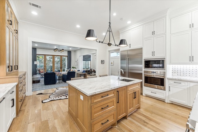 kitchen featuring a center island with sink, white cabinetry, built in appliances, and light stone counters