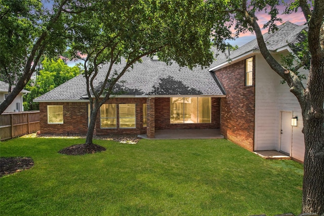 back house at dusk featuring a yard and a patio area