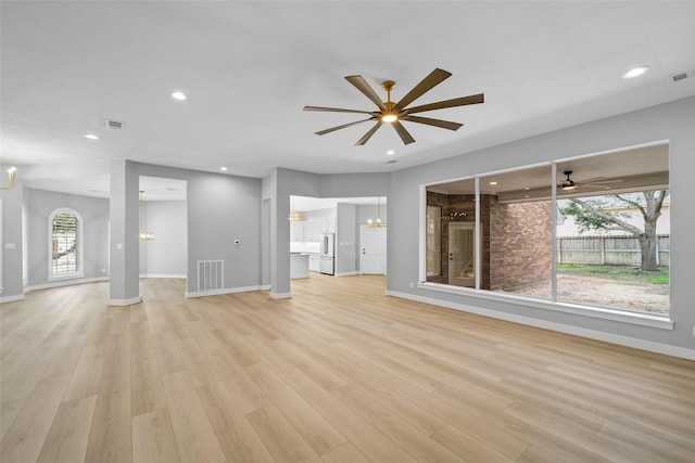 unfurnished living room with ceiling fan with notable chandelier and light hardwood / wood-style flooring