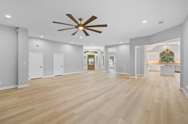 unfurnished living room with ceiling fan with notable chandelier and light hardwood / wood-style floors