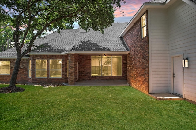 back house at dusk with a patio area and a lawn