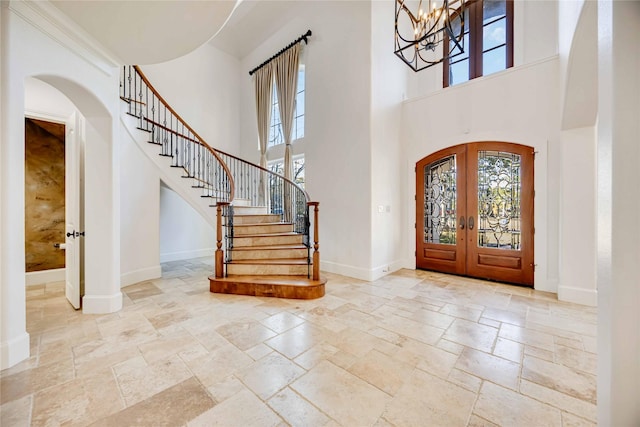 foyer entrance featuring an inviting chandelier, a towering ceiling, and french doors