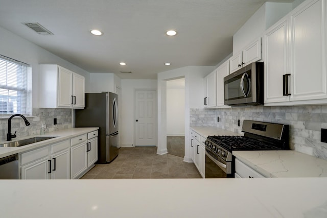 kitchen with light stone countertops, white cabinetry, appliances with stainless steel finishes, and sink