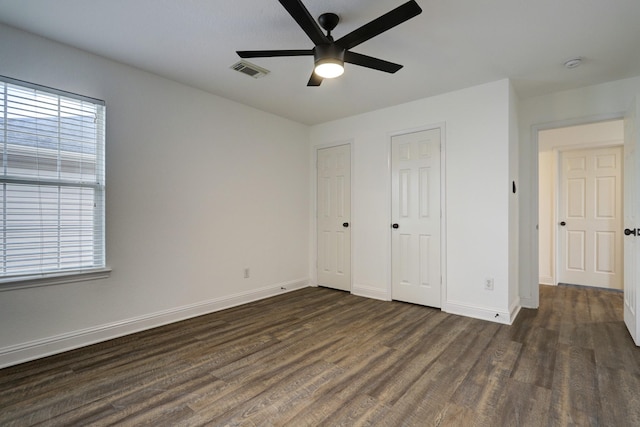 unfurnished bedroom featuring dark hardwood / wood-style floors, two closets, and ceiling fan