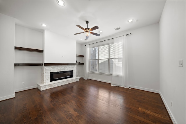 unfurnished living room with a stone fireplace, dark hardwood / wood-style floors, and ceiling fan