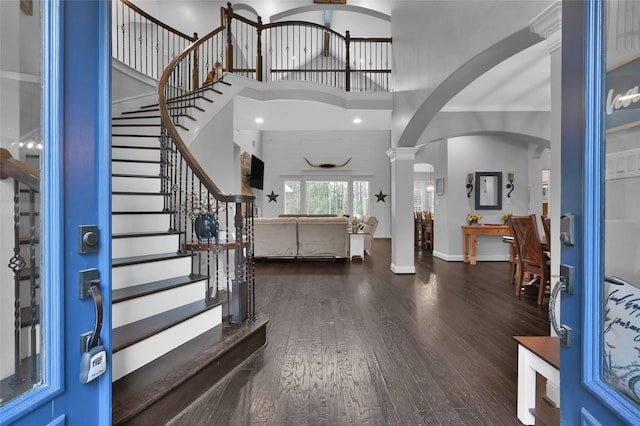 foyer entrance with decorative columns, dark hardwood / wood-style floors, and a towering ceiling