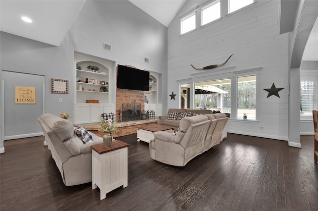 living room featuring a stone fireplace, dark wood-type flooring, lofted ceiling, and built in shelves