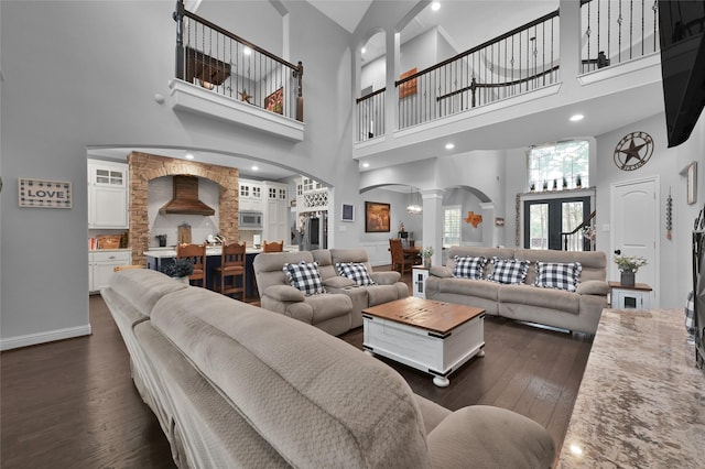 living room featuring dark wood-type flooring, a towering ceiling, and ornate columns