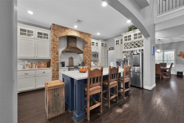 kitchen with appliances with stainless steel finishes, a kitchen island with sink, white cabinetry, custom range hood, and decorative light fixtures