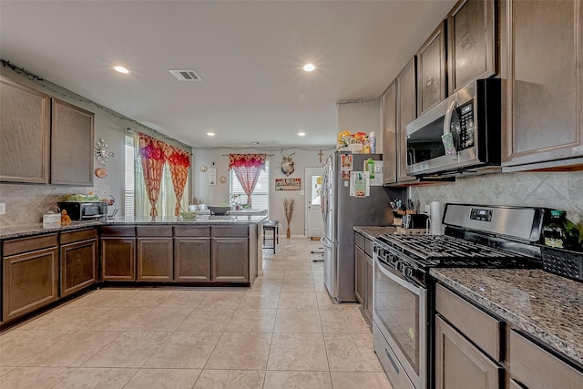 kitchen with light tile patterned flooring, decorative backsplash, dark stone counters, kitchen peninsula, and stainless steel appliances