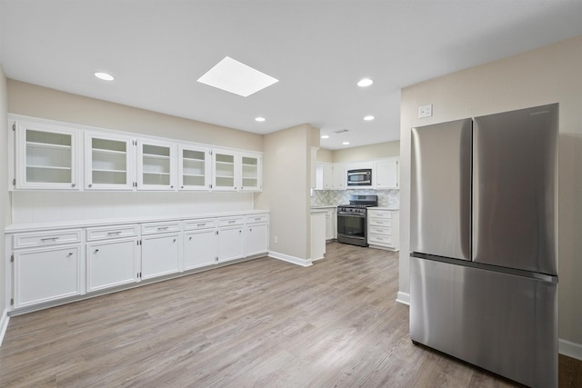 kitchen with stainless steel appliances, white cabinets, light hardwood / wood-style floors, and a skylight