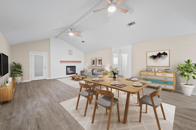 dining area with ceiling fan, vaulted ceiling with beams, a fireplace, and light hardwood / wood-style flooring