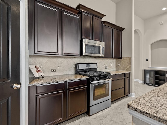 kitchen featuring decorative backsplash, dark brown cabinets, light tile patterned flooring, and appliances with stainless steel finishes