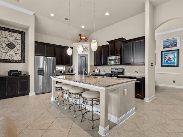 kitchen featuring light tile patterned flooring, appliances with stainless steel finishes, decorative light fixtures, light stone counters, and a center island with sink