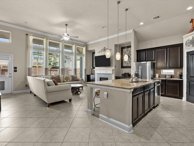 kitchen with pendant lighting, light tile patterned floors, light stone counters, an island with sink, and stainless steel fridge with ice dispenser