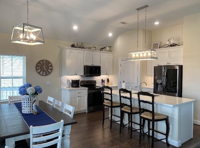 kitchen with decorative light fixtures, a center island with sink, stainless steel fridge, black range with electric cooktop, and white cabinets