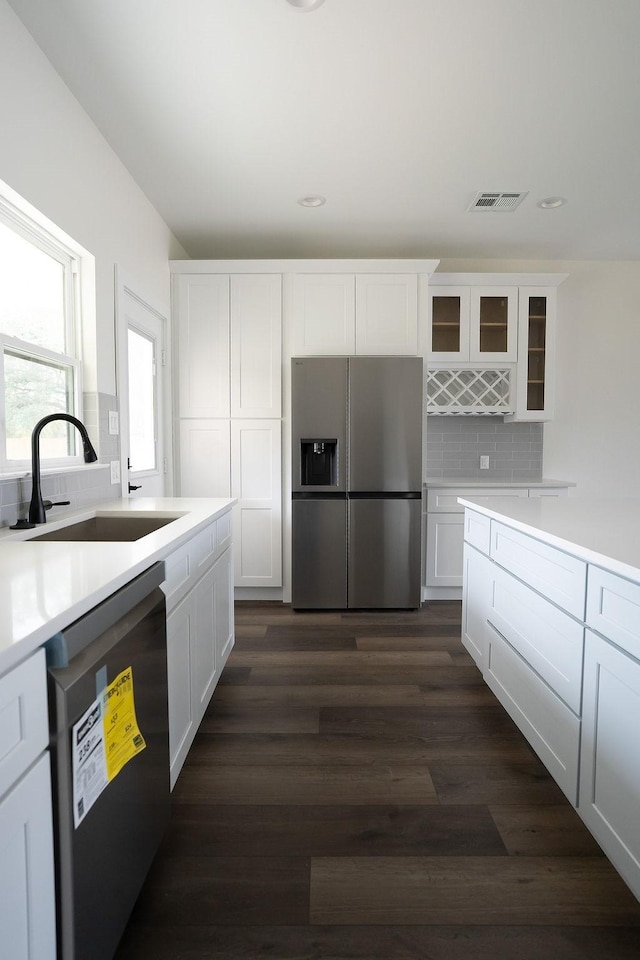 kitchen with white cabinetry, dishwashing machine, and stainless steel fridge