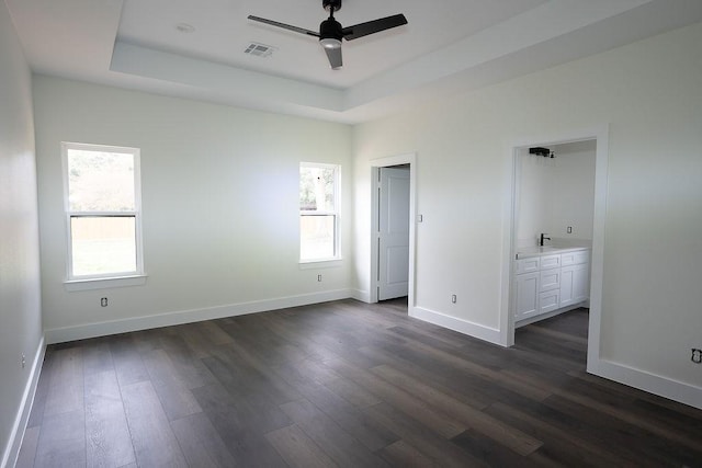 unfurnished bedroom featuring connected bathroom, a tray ceiling, and dark hardwood / wood-style floors