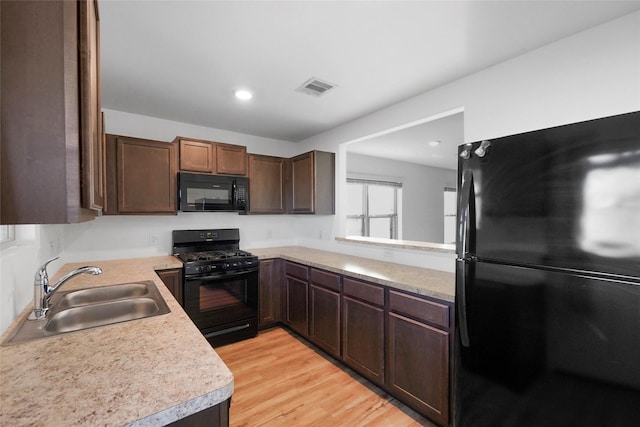 kitchen with dark brown cabinetry, sink, light wood-type flooring, and black appliances