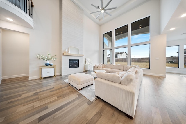 living room featuring ceiling fan, a towering ceiling, wood-type flooring, and a fireplace