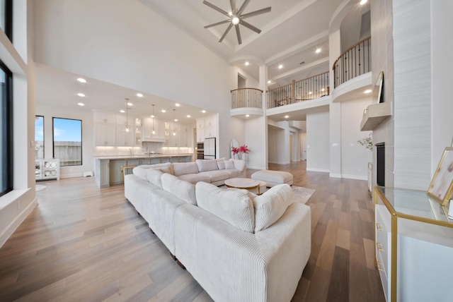 living room featuring a high ceiling, a large fireplace, ceiling fan, and light hardwood / wood-style flooring