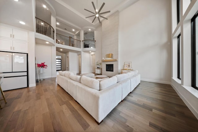 living room featuring a large fireplace, hardwood / wood-style floors, ceiling fan, and a towering ceiling