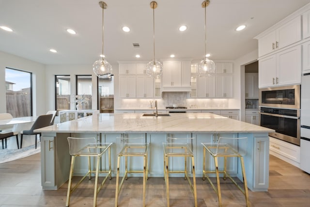 kitchen featuring a large island, sink, appliances with stainless steel finishes, white cabinetry, and hanging light fixtures