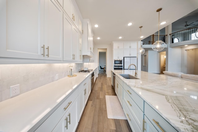 kitchen with sink, appliances with stainless steel finishes, hanging light fixtures, backsplash, and white cabinets