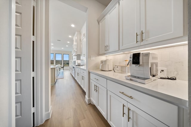 kitchen with tasteful backsplash, stainless steel gas stovetop, white cabinets, and light hardwood / wood-style floors