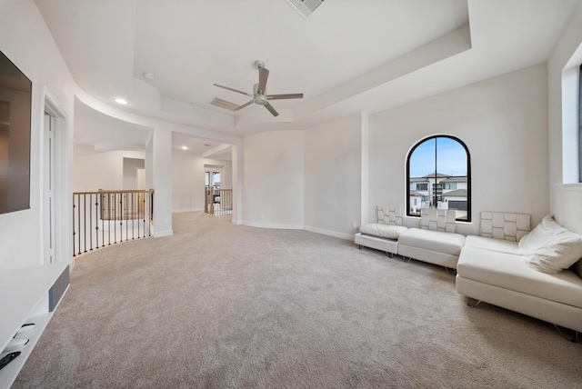 unfurnished living room featuring a tray ceiling, ceiling fan, and carpet flooring