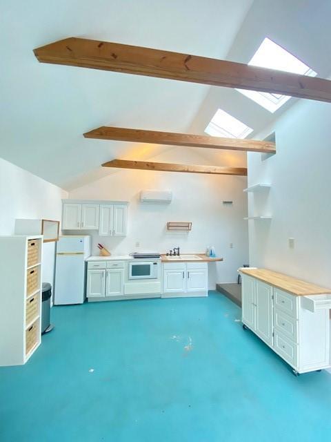 interior space featuring white cabinetry, wooden counters, vaulted ceiling with skylight, and white refrigerator